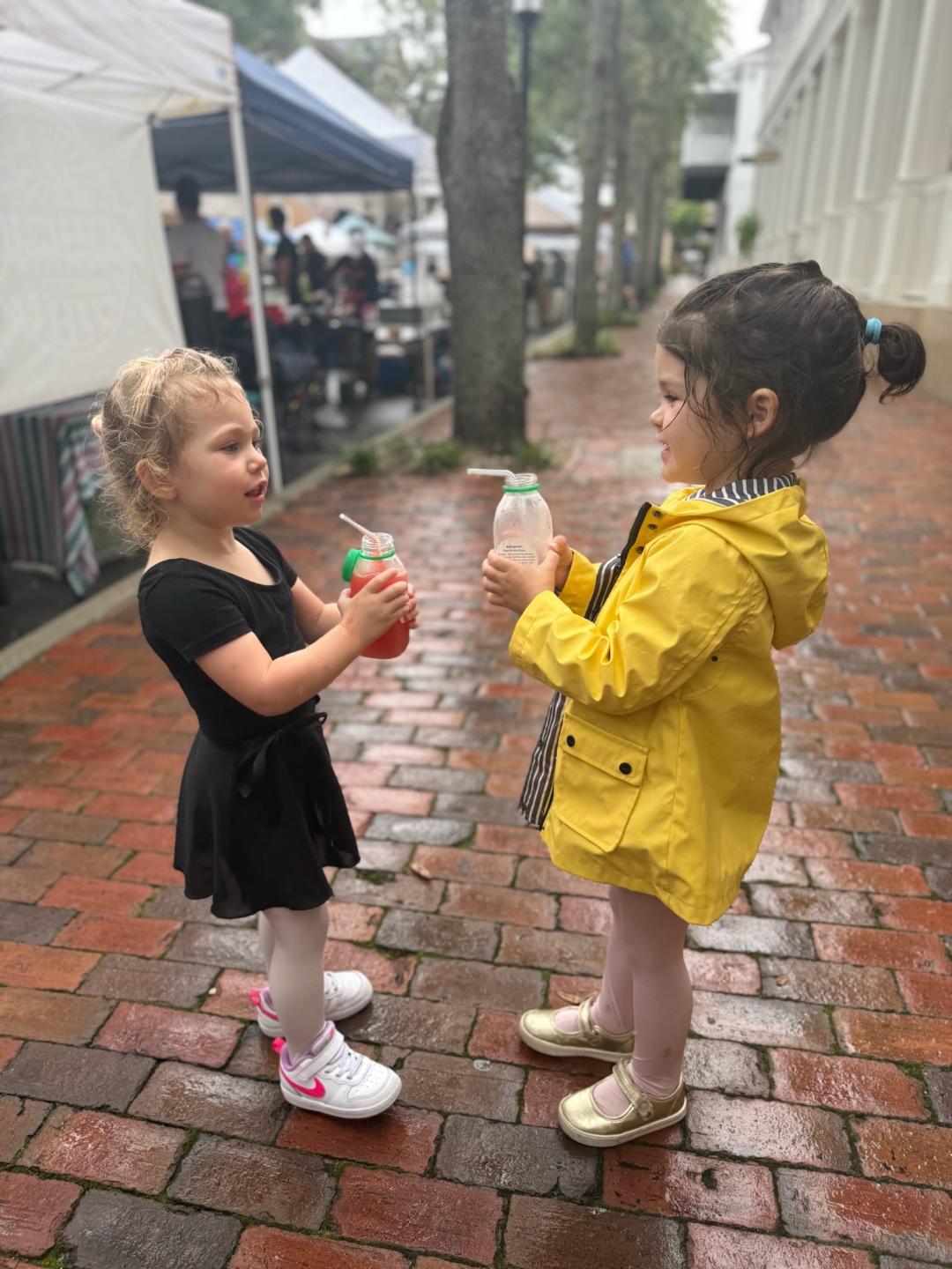 Two young children sharing Life in a Bottle juices at the farmers market